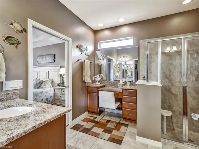 Full bath featuring connected bathroom, two vanities, a shower stall, and light tile patterned flooring