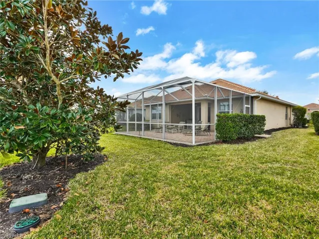Rear view of property with a sunroom, a lanai, a lawn, and stucco siding