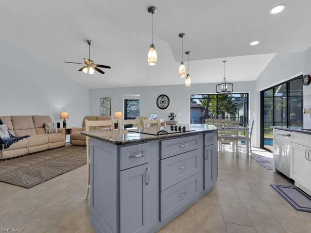 Kitchen with vaulted ceiling, dark stone countertops, hanging light fixtures, open floor plan, and a kitchen island