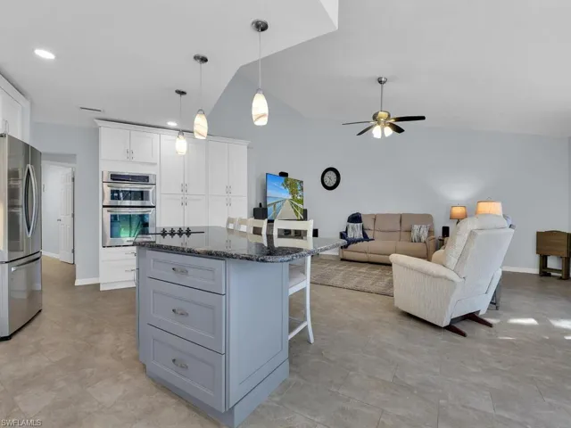 Kitchen featuring gray cabinets, pendant lighting, a kitchen bar, appliances with stainless steel finishes, and dark stone counters