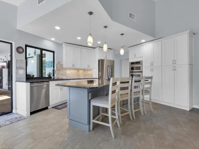 Kitchen featuring a kitchen breakfast bar, pendant lighting, appliances with stainless steel finishes, dark stone counters, and a center island