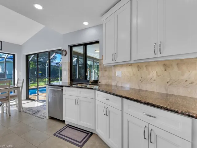 Kitchen featuring dark stone countertops, white cabinetry, stainless steel dishwasher, tasteful backsplash, and lofted ceiling