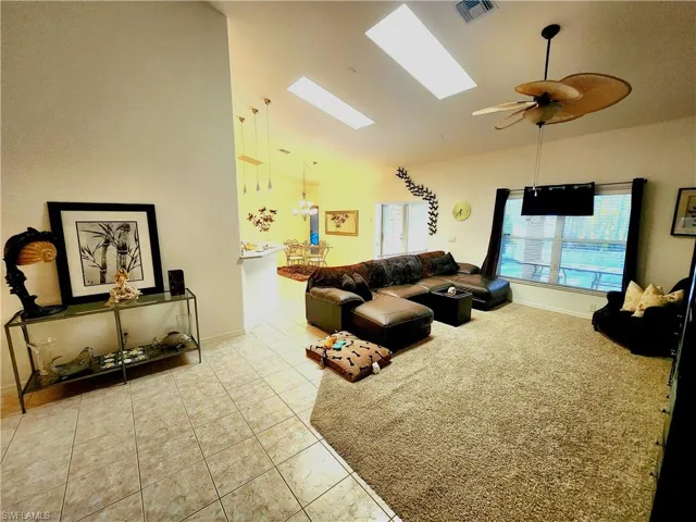 Living room with vaulted ceiling, light tile patterned floors, a skylight, and ceiling fan