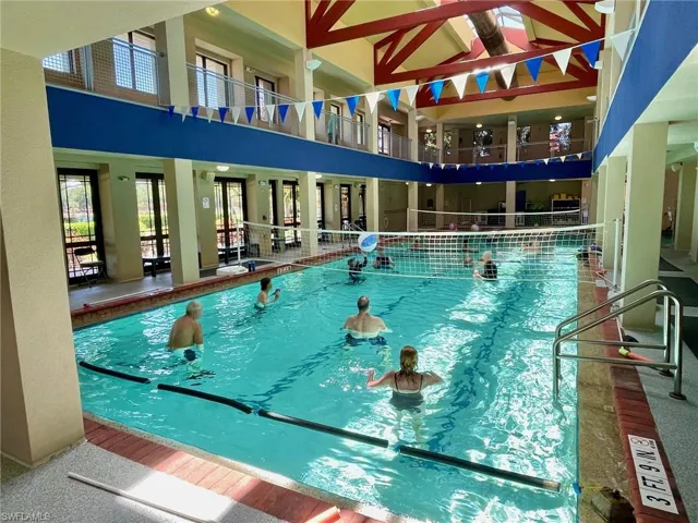 Indoor swimming pool featuring a volleyball net, overhead skylights, and multi-level architectural design with walking track balcony