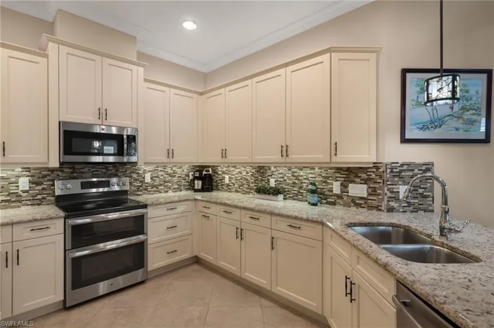 Kitchen featuring appliances with stainless steel finishes, pendant lighting, sink, ornamental molding, and light stone counters