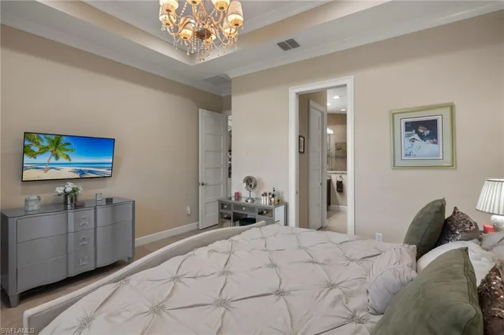 Bedroom featuring ensuite bathroom, a notable chandelier, ornamental molding, light colored carpet, and a raised ceiling