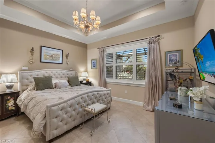 Tiled bedroom with crown molding, a notable chandelier, and a tray ceiling