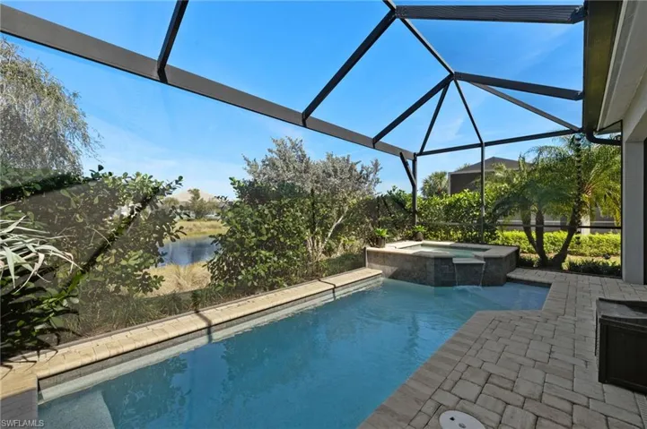 View of pool with an in ground hot tub, a water view, a patio area, and glass enclosure