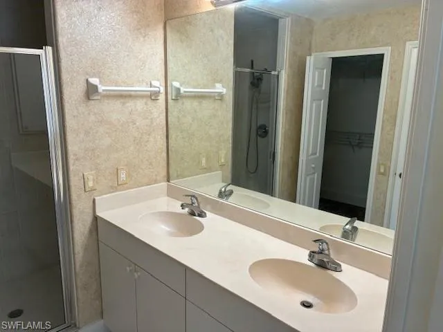 Bathroom featuring a shower stall, double vanity, a spacious closet, and a textured wall