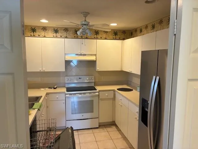 Kitchen with white range with electric cooktop, light countertops, stainless steel fridge with ice dispenser, decorative backsplash, and white cabinets