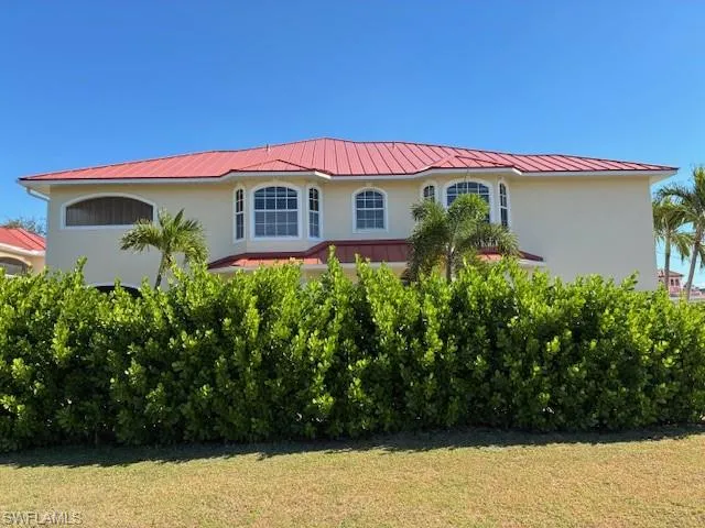 View of front of home with stucco siding, a front yard, and a metal roof