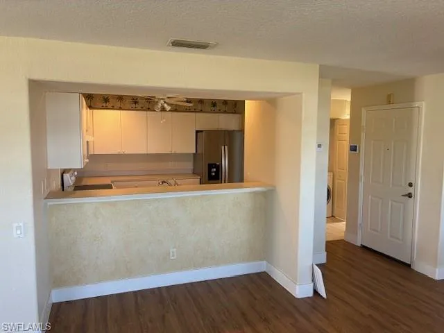 Kitchen featuring stainless steel fridge, light countertops, stove, dark wood finished floors, and a textured ceiling