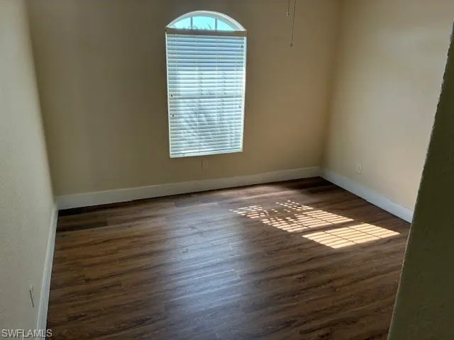 Spare room with dark wood-style flooring and baseboards