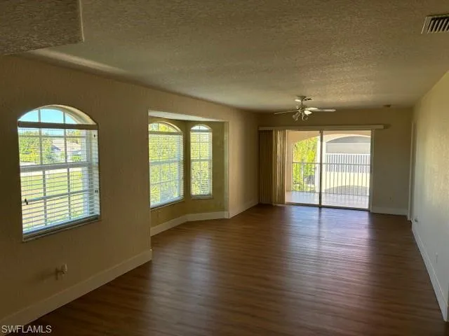Unfurnished room featuring a textured wall, a textured ceiling, dark wood-type flooring, and ceiling fan