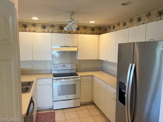 Kitchen featuring stainless steel fridge, white electric range oven, light countertops, tasteful backsplash, and white cabinets