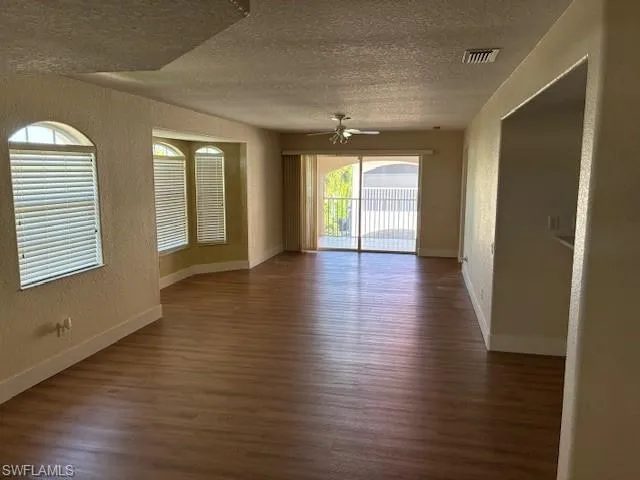 Spare room featuring a textured wall, dark wood-style floors, a textured ceiling, and ceiling fan