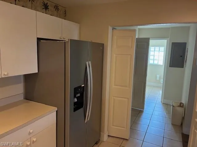 Kitchen featuring light countertops, white cabinetry, stainless steel refrigerator with ice dispenser, electric panel, and light tile patterned flooring