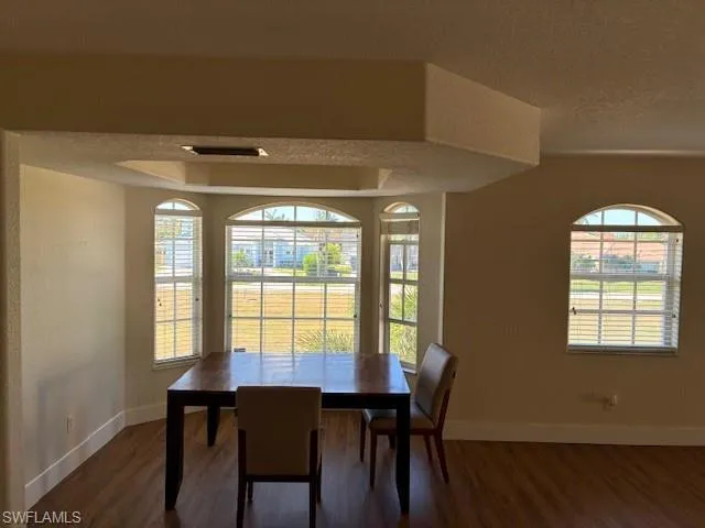 Dining area with a textured wall, a textured ceiling, plenty of natural light, and dark wood-type flooring