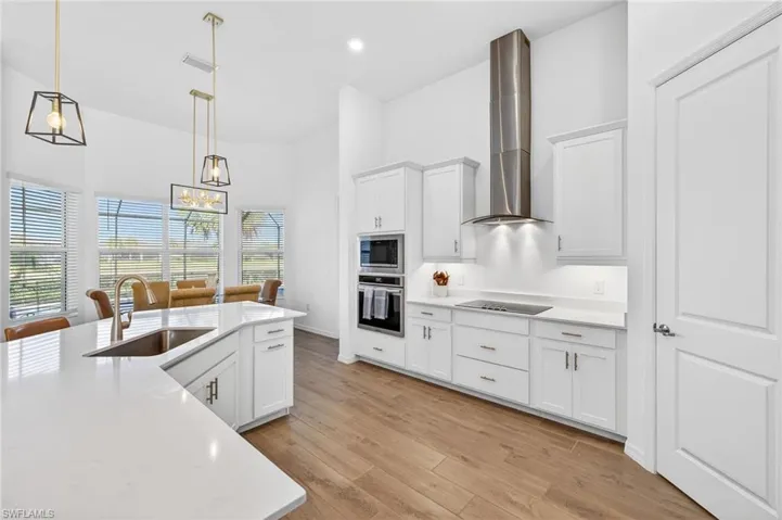 Kitchen with appliances with stainless steel finishes, white cabinets, wall chimney range hood, pendant lighting, and light wood-type flooring