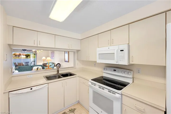 Kitchen featuring cream cabinetry, white appliances, light countertops, light tile patterned flooring, and ceiling fan