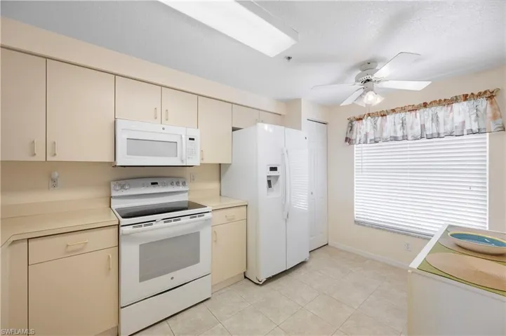 Kitchen featuring light countertops, a textured ceiling, light tile patterned floors, white appliances, and cream cabinets
