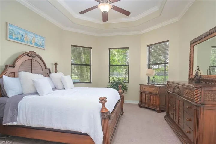 Carpeted bedroom featuring ceiling fan, a tray ceiling, and ornamental molding
