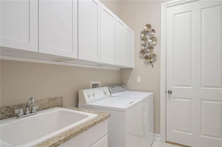 Laundry area with washer and clothes dryer, light tile patterned floors, cabinets, and sink