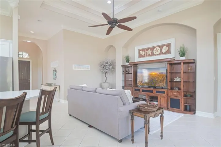 Living room with ceiling fan, light tile patterned floors, and crown molding