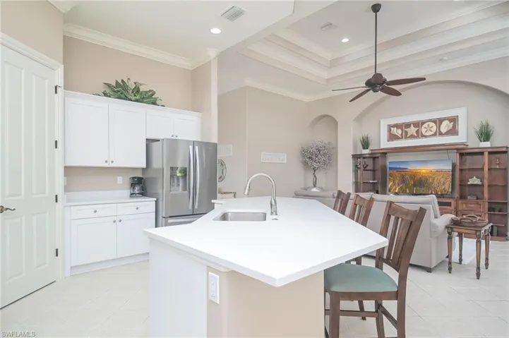 Kitchen featuring stainless steel fridge, a kitchen island with sink, sink, and white cabinets