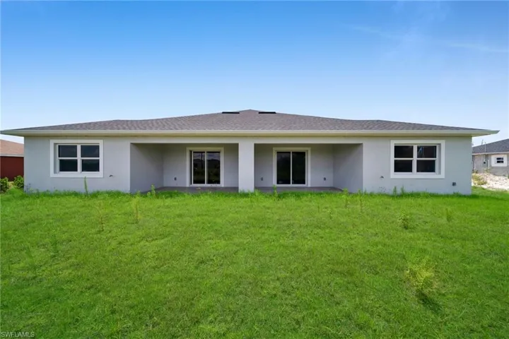 Rear exterior featuring a covered patio, dual sliding glass doors, white-framed windows, a shingle roof, and a green lawn area