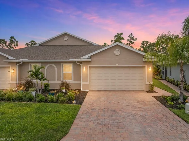 Stucco exterior with a paver driveway, an attached garage, and a landscaped front yard
