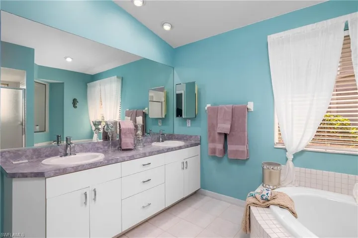 Bathroom with tiled bath, oversized vanity, dual sinks, and tile floors