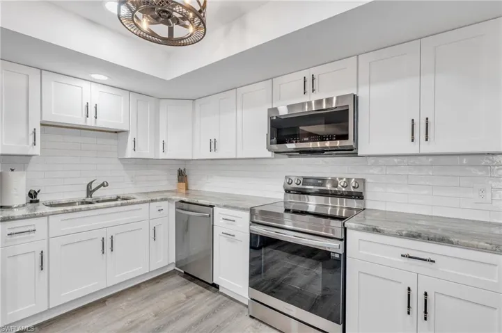 Kitchen with tasteful backsplash, stainless steel appliances, white cabinetry, sink, and light hardwood / wood-style floors