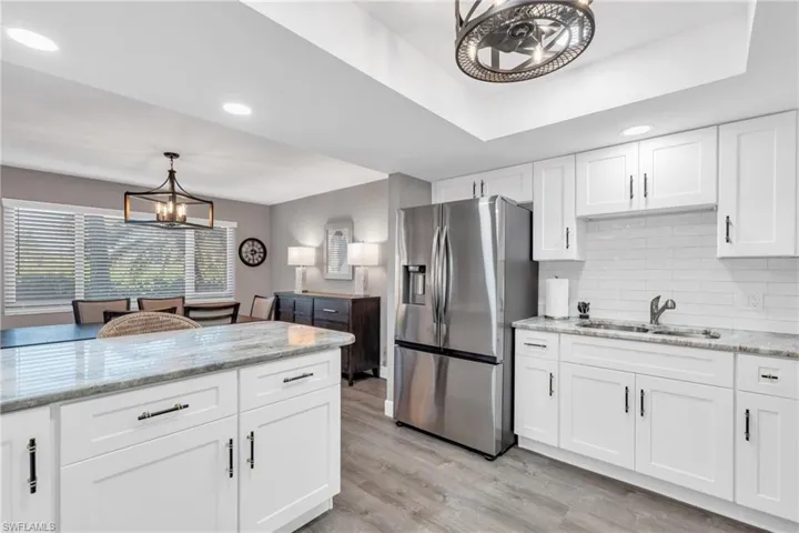 Kitchen with white cabinets, sink, stainless steel fridge with ice dispenser, light wood-type flooring, and decorative light fixtures