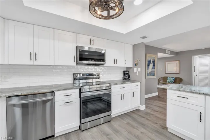 Kitchen with stainless steel appliances, white cabinets, tasteful backsplash, light stone countertops, and light hardwood / wood-style flooring