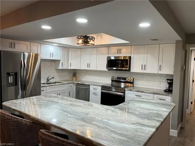 Kitchen with white cabinets, hardwood / wood-style flooring, sink, backsplash, and appliances with stainless steel finishes