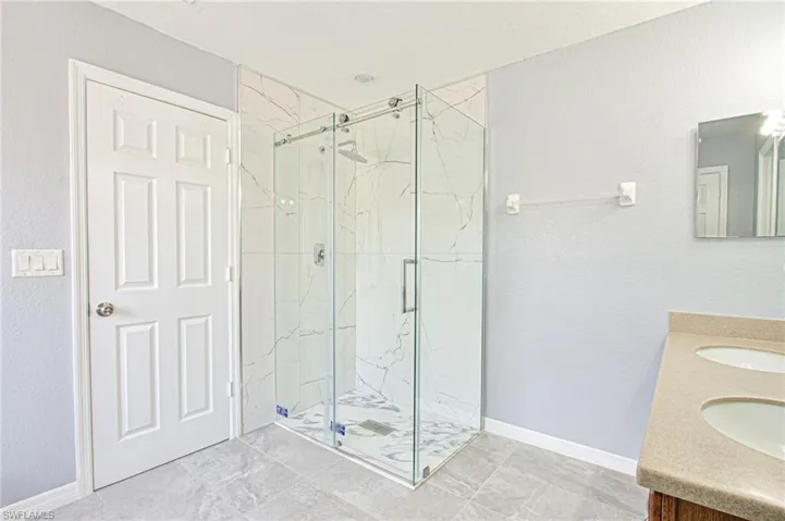 Full bathroom featuring a textured wall, a marble finish shower, and double vanity