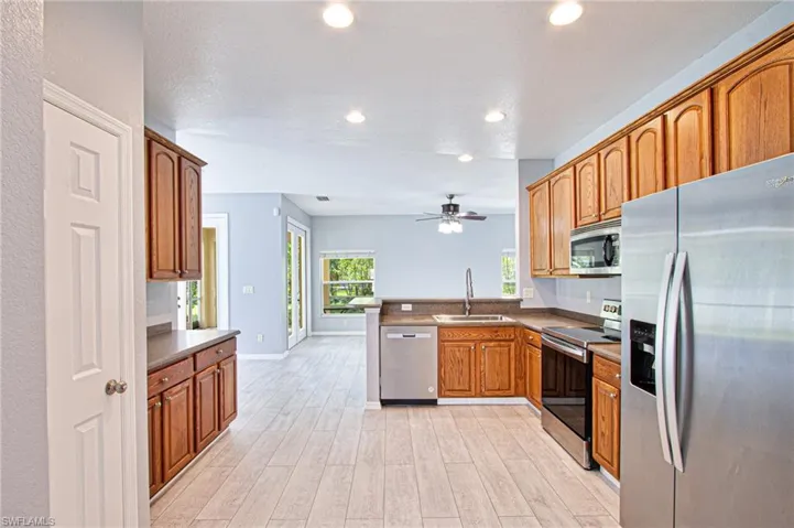Kitchen with appliances with stainless steel finishes, a peninsula, dark countertops, light wood-style flooring, and recessed lighting