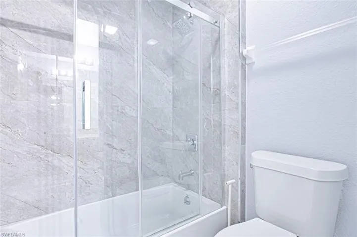 Full bath with a textured wall and combined bath / shower with glass door