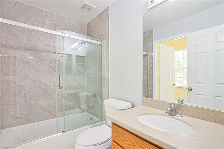 Bathroom featuring enclosed tub / shower combo, vanity, and a textured wall