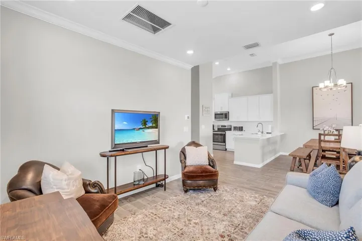 Living area featuring visible vents, crown molding, baseboards, a chandelier, and light wood-type flooring