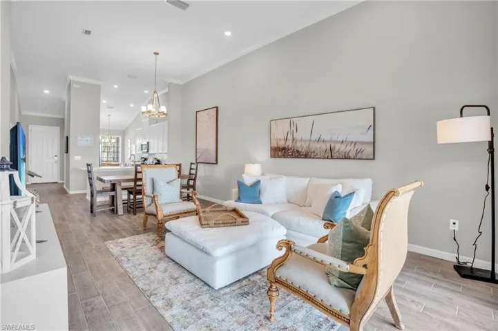Living area featuring wood finish floors, baseboards, a chandelier, and crown molding