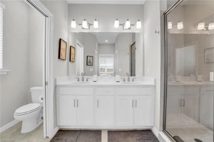 Full bathroom with double vanity, a shower stall, toilet, and a sink
