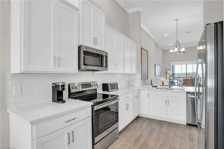 Kitchen with backsplash, crown molding, a chandelier, appliances with stainless steel finishes, and a sink