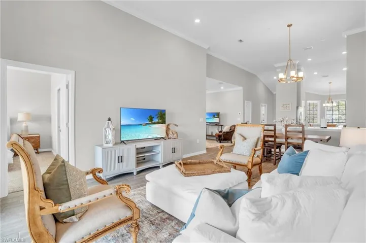Living room with baseboards, an inviting chandelier, light wood-style flooring, lofted ceiling, and ornamental molding