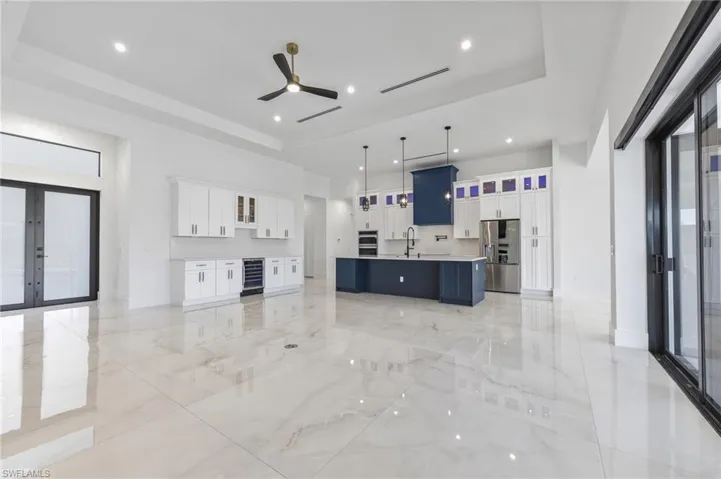 Open-concept kitchen featuring high-gloss large-format tile flooring, white cabinetry with contrasting dark-toned central island, stainless steel built-in appliances, and recessed lighting with tray ceiling detail