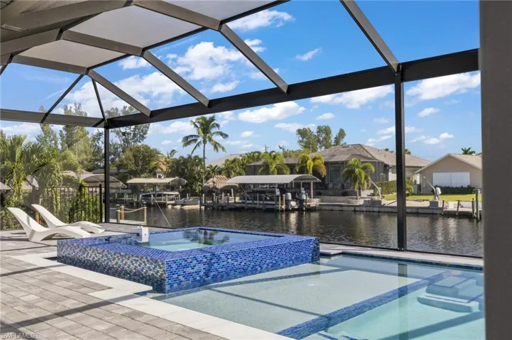 Screened-in pool area featuring an elevated tiled spa, concrete paver decking, and direct bulkhead water access