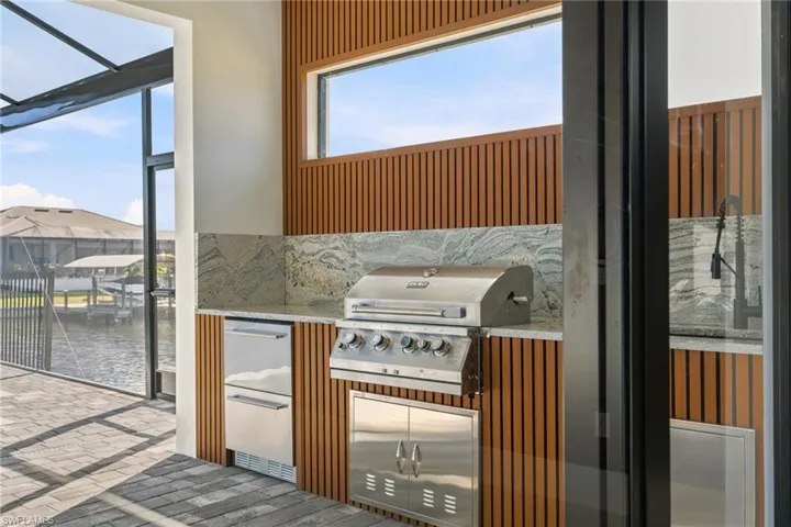 Outdoor kitchen featuring stone countertops, built-in stainless steel grill, stainless steel under-counter refrigeration, and slatted wood wall paneling