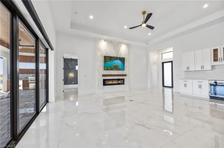 Large-format stone tile flooring, floor-to-ceiling multi-panel sliding glass doors, coffered ceiling, linear fireplace with stone hearth, and white shaker-style built-in cabinetry