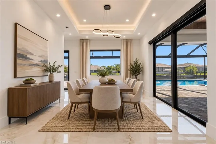 Dining area featuring a tray ceiling with recessed lighting, a modern multi-ring chandelier, large format polished tile flooring, and floor-to-ceiling sliding glass doors opening to a screened pool enclosure